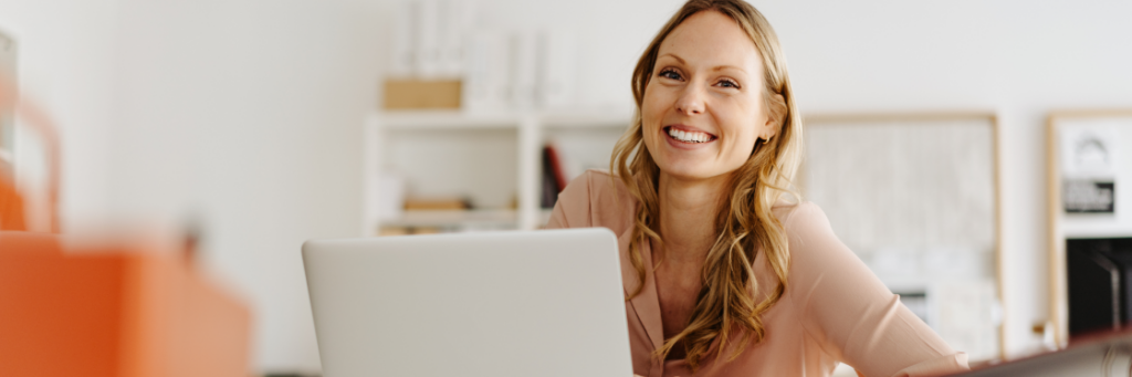 Smiling woman using Biteable video maker on a laptop in a bright office setting.