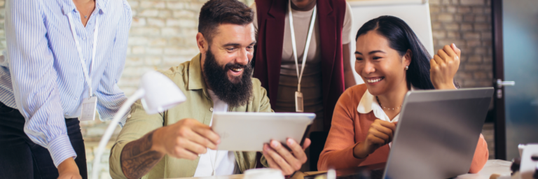 A diverse group of professionals enthusiastically discussing over digital tablets and a laptop in a modern office setting, utilizing Biteable video maker.