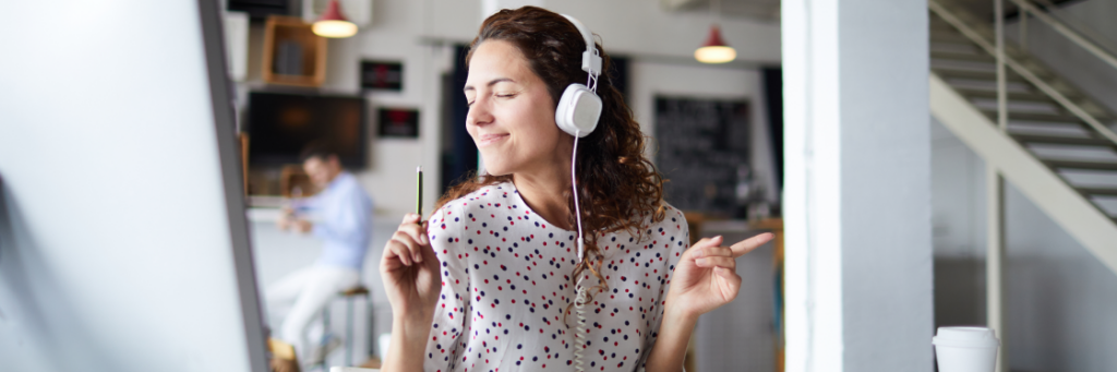 A woman wearing headphones enjoys music with permission to use a song while working in a modern office space.