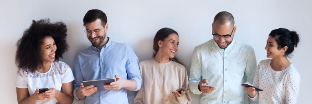 Group of five diverse friends smiling and looking at their phones and a tablet, exploring different types of social media.