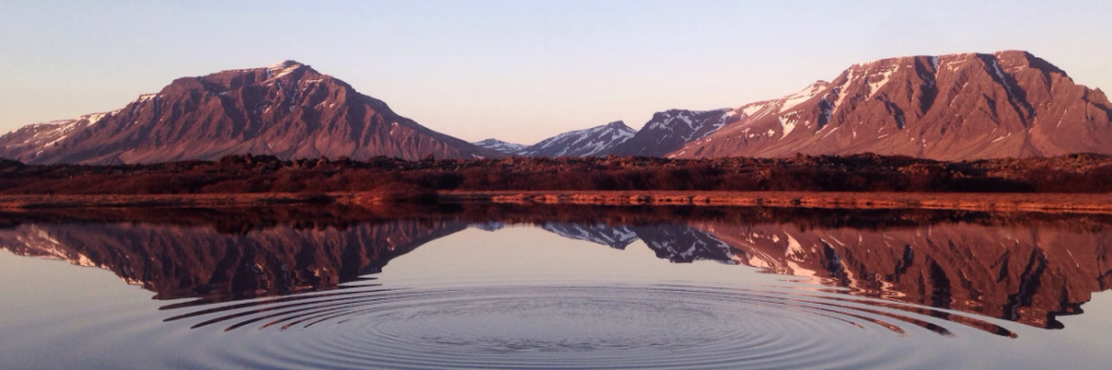 Mountains reflected in a calm lake with a single ripple on the water's surface.