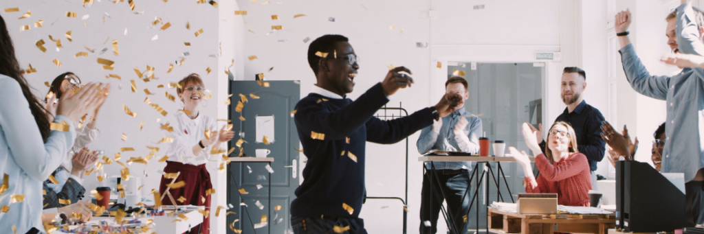 A group of office workers celebrating an improved click-through rate with confetti and applause in a brightly lit room.