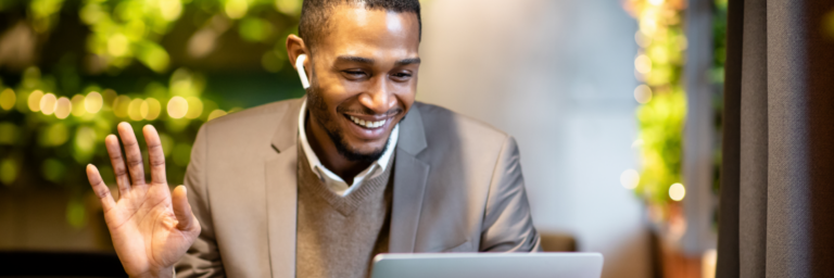 A smiling person in professional attire using earbuds while gesturing a greeting or acknowledgement during a video call on a laptop, created with Biteable video maker.