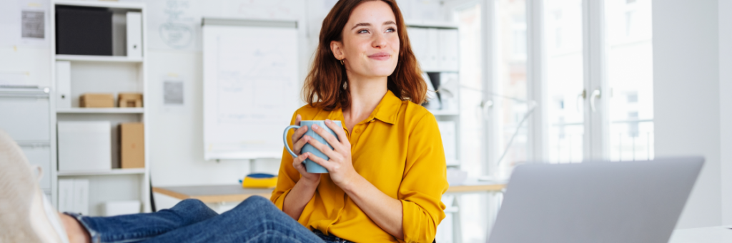 Woman in yellow blouse holding a cup and looking away thoughtfully in an office environment.