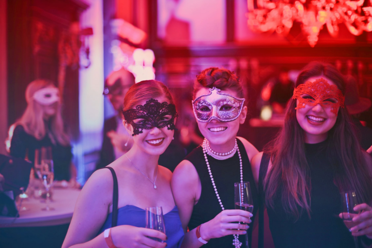 Three women at a masquerade party holding champagne flutes.