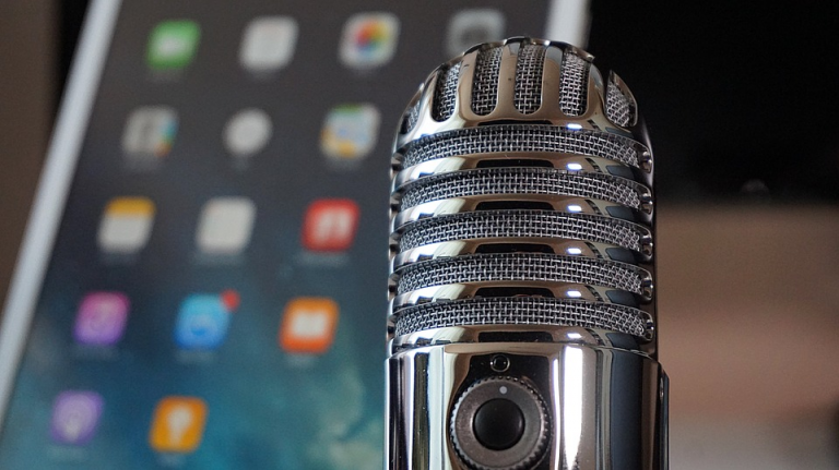 A vintage microphone in sharp focus with a blurred tablet screen in the background.