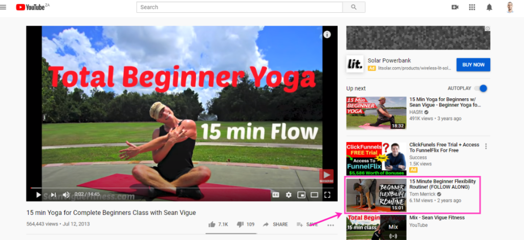 A screenshot of a youtube video titled "15 min yoga for complete beginners class with sean vigue," showing a man demonstrating a yoga pose on a mat outdoors.
