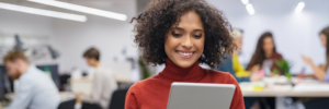 Woman smiling at tablet screen in a modern office environment.