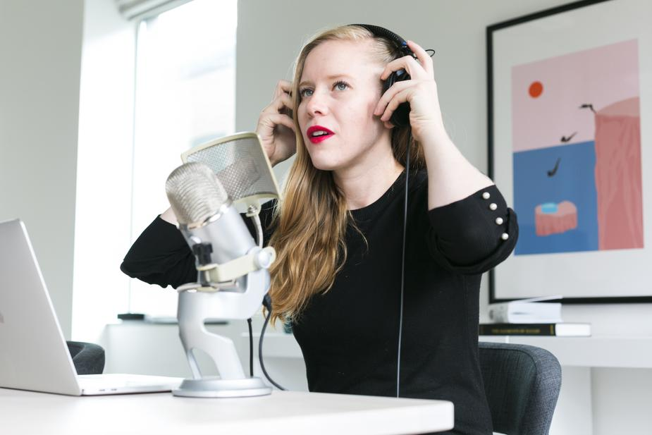 Woman recording a podcast or broadcasting with a microphone and headphones in a modern office setup.