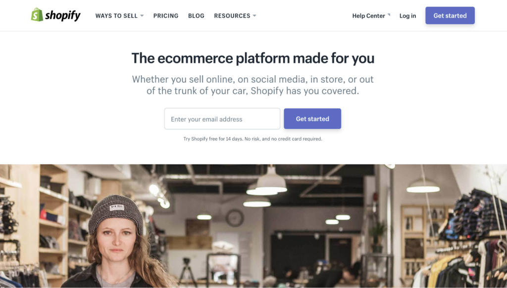 A woman standing in a store with shopify's homepage visible in the foreground, showcasing its e-commerce service offerings.