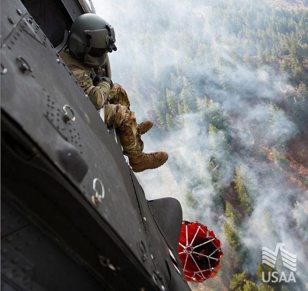 A soldier looks out from a helicopter performing a wildfire suppression mission.