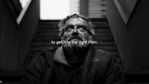 Black and white photo of a bearded man looking upward with a caption "to get it to the right man" displayed, sitting on steps in an urban setting, created using Biteable video maker.