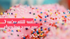 Close-up of a pink frosted donut sprinkled with colorful nonpareils, designed using Biteable video maker, with a text overlay that reads "you're still not showing your age.