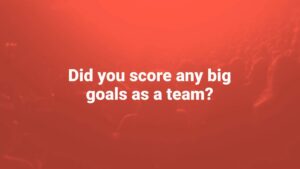 Silhouetted audience in a red-tinted light with the text "did you score any big goals as a team?" displayed over the image, created using Biteable video maker.