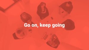 Overhead view of a meeting with four individuals around a table, image tinted in red with text "go on, keep going" created using Biteable video maker.