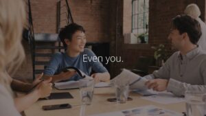 Three colleagues engaged in a friendly discussion at a meeting with the phrase "even you." displayed on the screen, created using Biteable video maker.