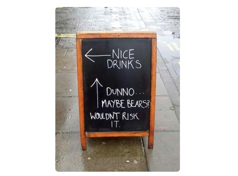 A sidewalk chalkboard sign with humorous directions: left arrow pointing to "nice drinks" and an upward arrow with "dunno... maybe bears? wouldn't risk it for a Biteable video.