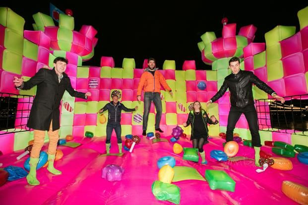 Five people jumping joyfully on a colorful inflatable playground at night, illuminated by bright lights from a Biteable video maker.