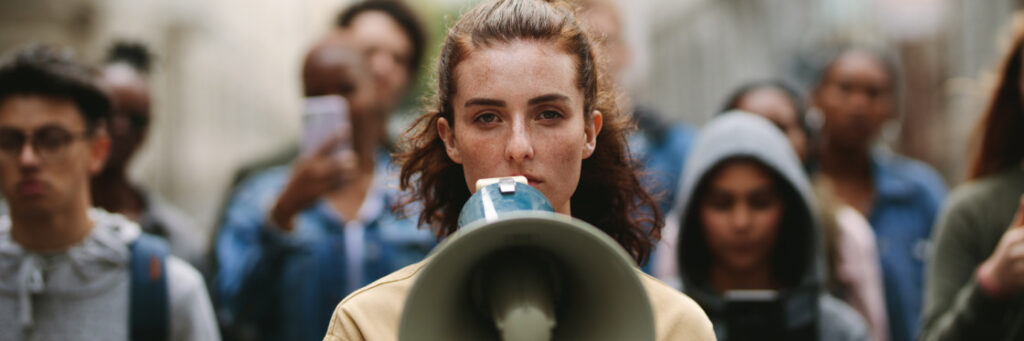 A woman with a megaphone stands in focus amidst a blurry crowd, symbolizing leadership or activism in a Biteable video.