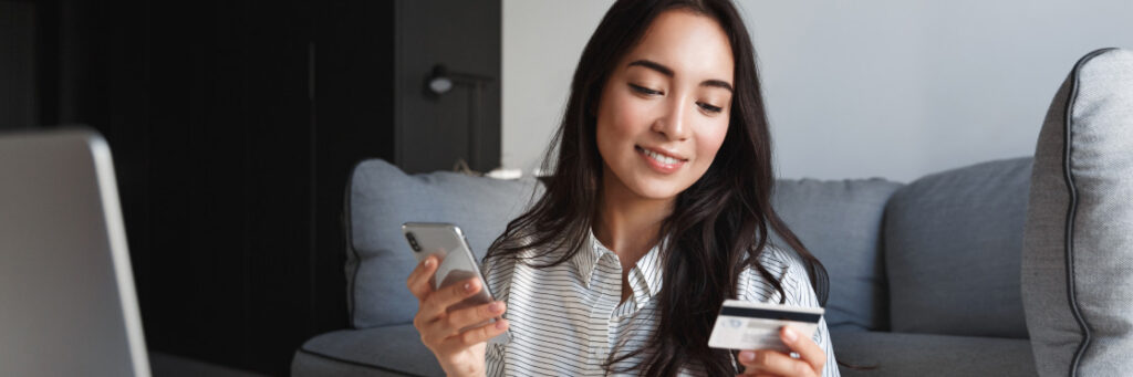 Woman sitting on a couch, holding a smartphone and a credit card, possibly shopping online or managing finances using Biteable video maker.