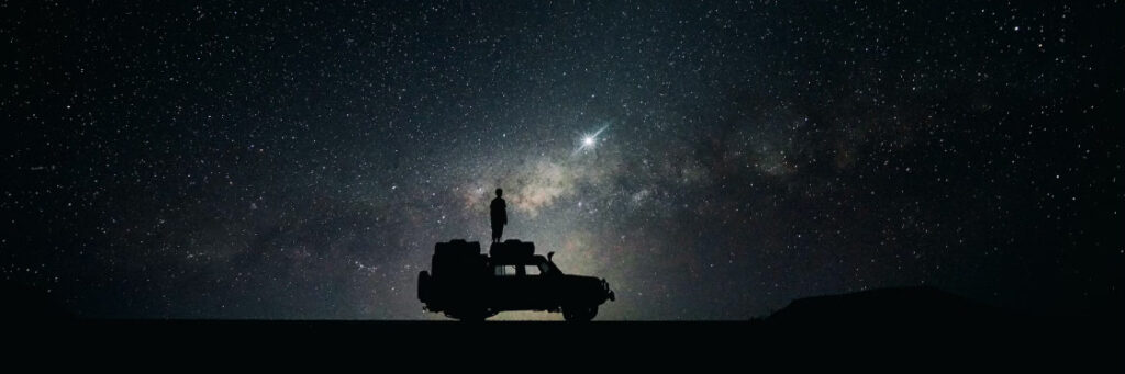 A silhouette of a person standing on a vehicle under a starry sky with a visible shooting star, perfect for capturing in a Biteable video.