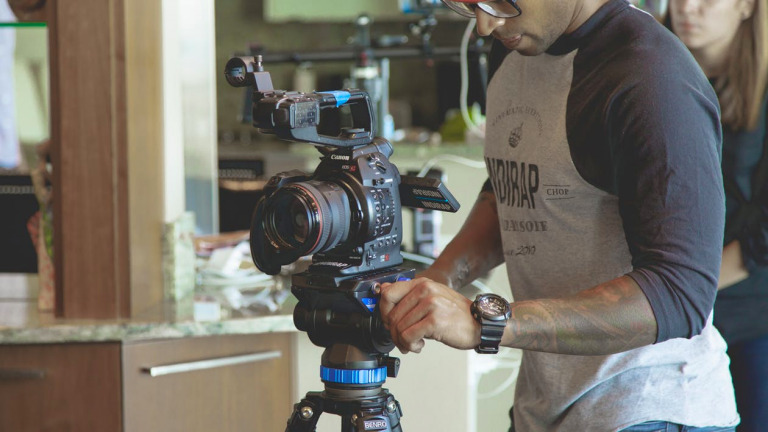 Man adjusting a Biteable video maker camera mounted on a tripod indoors, focusing on the equipment's settings.