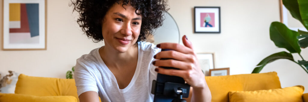 Woman with curly hair smiles while taking a photo with a camera in a cozy living room setting using Biteable video maker.