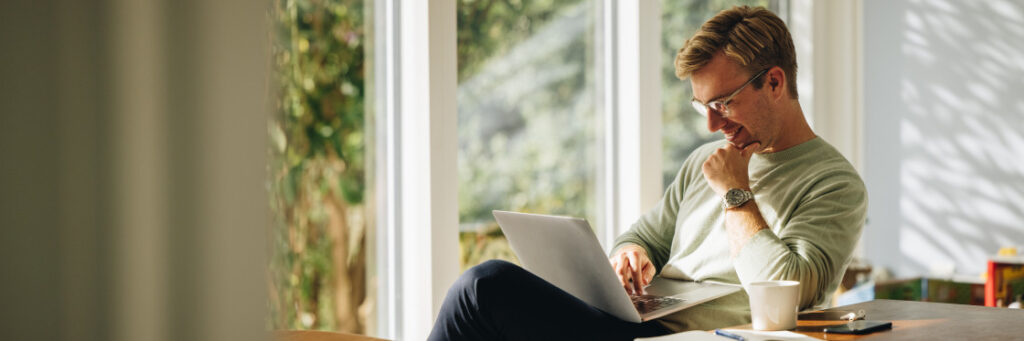 Man sitting at a table in a sunlit room working on a Biteable video maker with a coffee cup beside him.