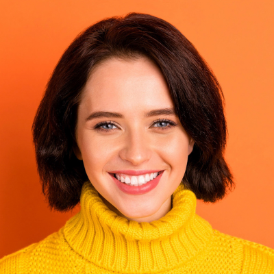 A smiling woman with short brown hair wearing a yellow turtleneck, against an orange background.