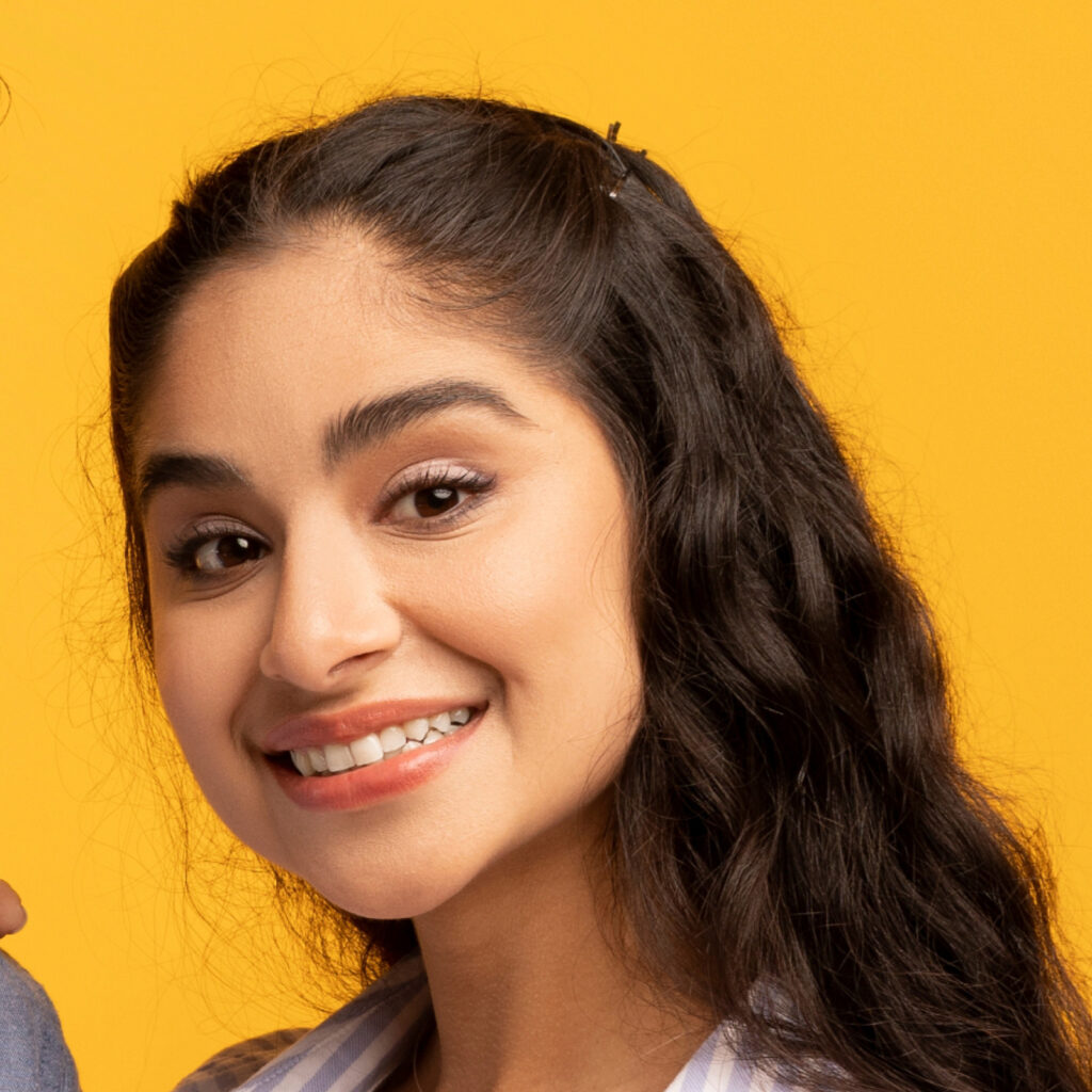 Young woman with long wavy hair and a subtle smile, wearing a light blouse, against a yellow background.