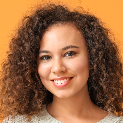 Portrait of a smiling young woman with curly hair against an orange background.