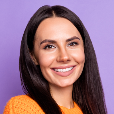 A smiling woman with long, dark hair wearing an orange sweater, against a purple background.