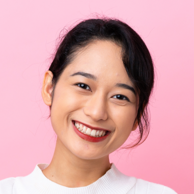 Portrait of a smiling young Asian woman with long hair, wearing a white top, against a pink background.