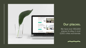 A laptop displaying accommodation listings sits on a white desk next to a clear glass holding a green leaf; text highlights over 650,000 stays in 2,000+ cities worldwide.
