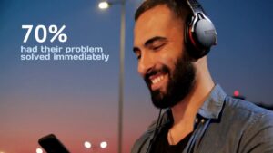 A man with headphones smiles at his phone outdoors at dusk. Text reads: "70% had their problem solved immediately.
