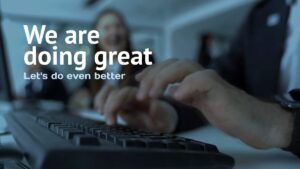 Close-up of hands typing on a keyboard with blurred people in the background and the text "We are doing great. Let's do even better" overlaid.