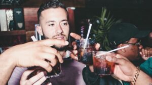 Several people holding up drinks with straws, appearing to make a toast in a dimly lit bar or club.