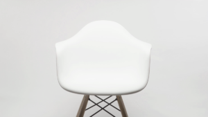 A modern white plastic armchair with wooden legs and a metal cross-brace, positioned against a plain white background.
