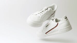 A pair of white Adidas sneakers with black and red accents, floating against a plain light background.