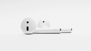 A pair of white wireless earbuds are placed on a plain white surface with a minimalist background.