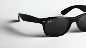 A pair of black Ray-Ban sunglasses with dark lenses resting on a white surface.