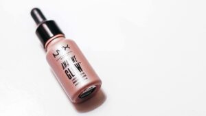 A bottle of NYX Professional Makeup Away We Glow liquid highlighter with a dropper lid rests on a white surface.