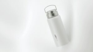 A white stainless steel water bottle with a metal lid and handle, placed on a white surface. The bottle has the word "Alliance" printed vertically.