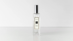 A clear glass bottle of Jo Malone cologne with a silver cap, placed upright on a white surface against a plain white background.