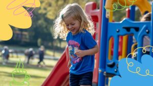 A young child with blonde hair wearing a blue shirt plays outside on playground equipment, with colorful doodles and blurred people in the background.