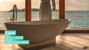 A person in a white robe stands by a modern bathtub facing large windows with a view of the ocean at sunset; overlaid text reads “Luxe 2012–2014 Digital marketer.”.